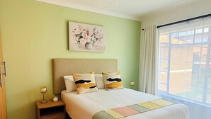 Quarto com cama, mesa de cabeceira, abajur e uma obra de arte na parede.