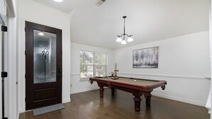 Een kamer met een pooltafel, een deur met geëtst glas, een raam en een schilderij aan de muur.