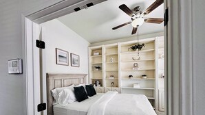 Een slaapkamer met een bed, een plafondventilator, een boekenplank en een deur.