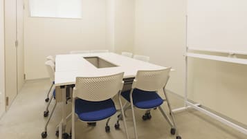 Una sala conferenze con un tavolo bianco, quattro sedie con cuscini blu, una lavagna e un orologio appeso al muro.