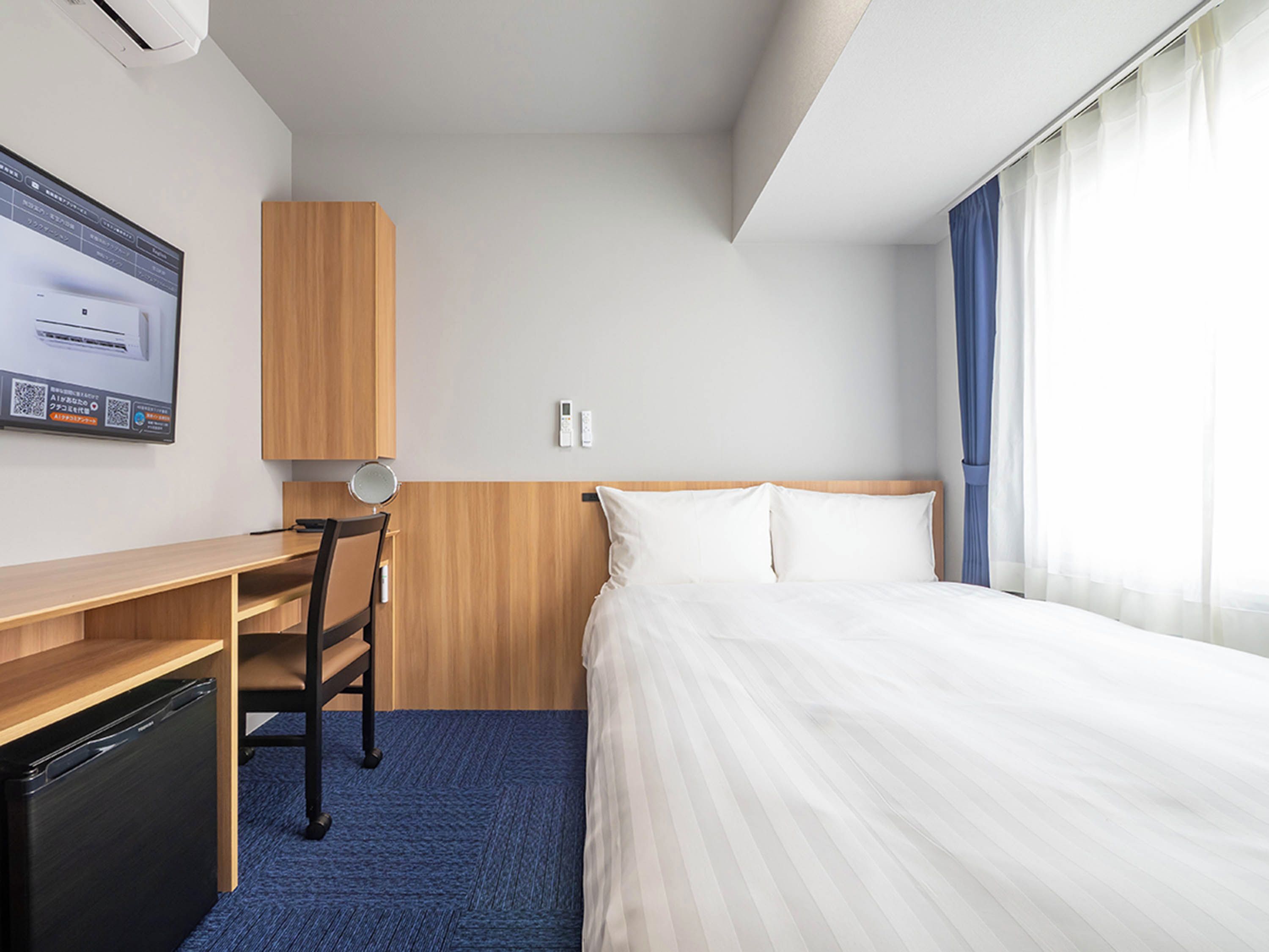 A hotel room with a bed, a desk, a chair, a TV, and a window with curtains.
