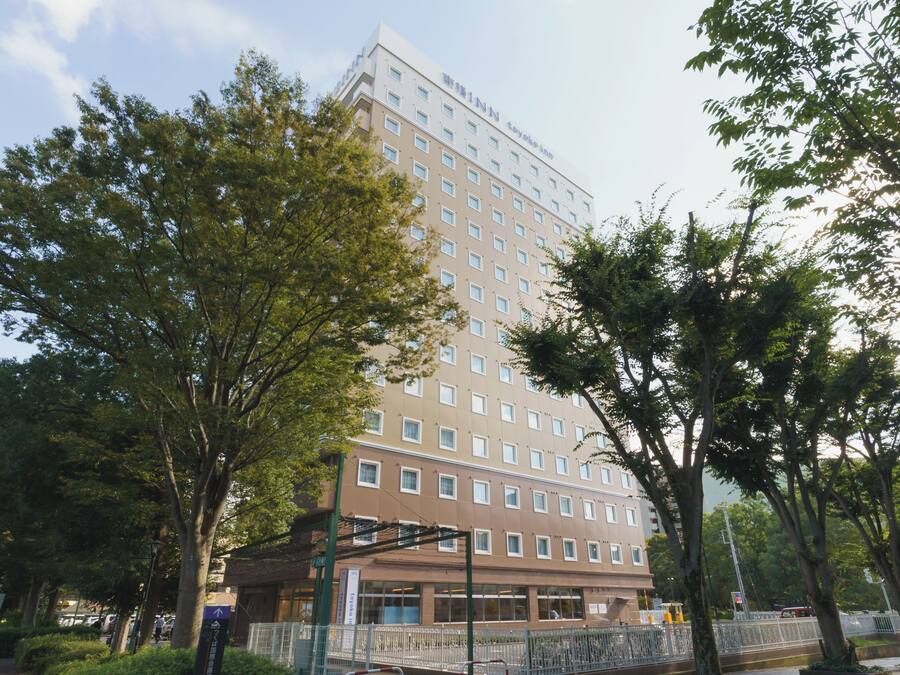 Hotel de varios pisos con diseño moderno, rodeado de árboles y una zona delimitada por una cerca.