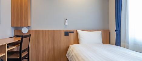 Una habitación de hotel con cama, escritorio, silla, luz en la pared y ventana con cortinas.