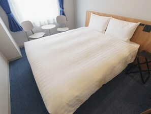 A hotel room with a large bed, two white chairs, a small table, and a wooden headboard. - Toyoko Inn Tsukuba-eki (Tsukuba)