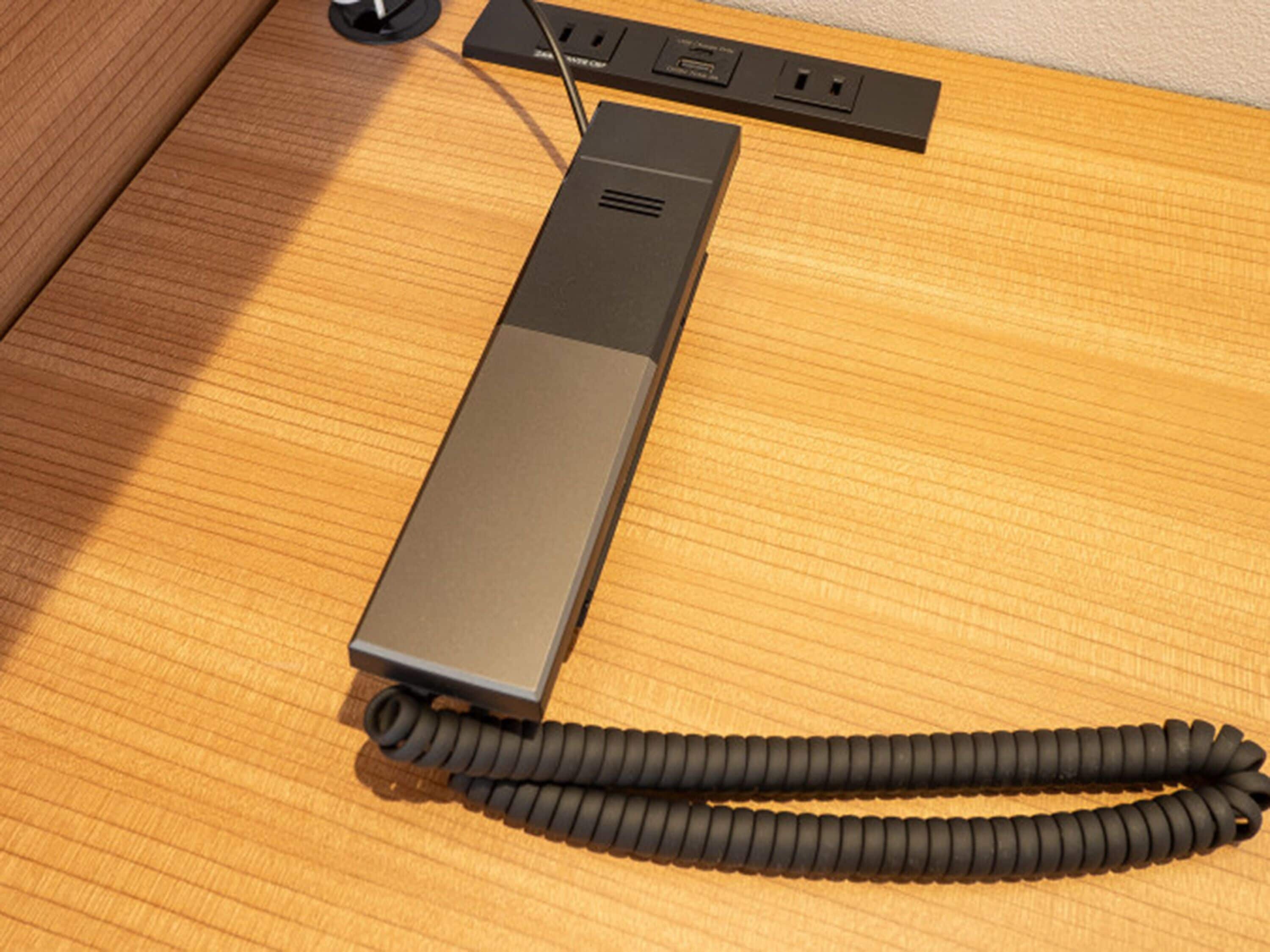 Teléfono negro con cable enrollado sobre una superficie de madera.