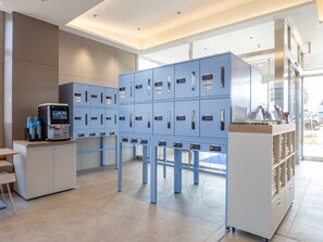 A modern hotel lobby with a coffee machine, a seating area, and a large blue storage unit with multiple compartments. - Toyoko Inn Tsukuba-eki (Tsukuba)