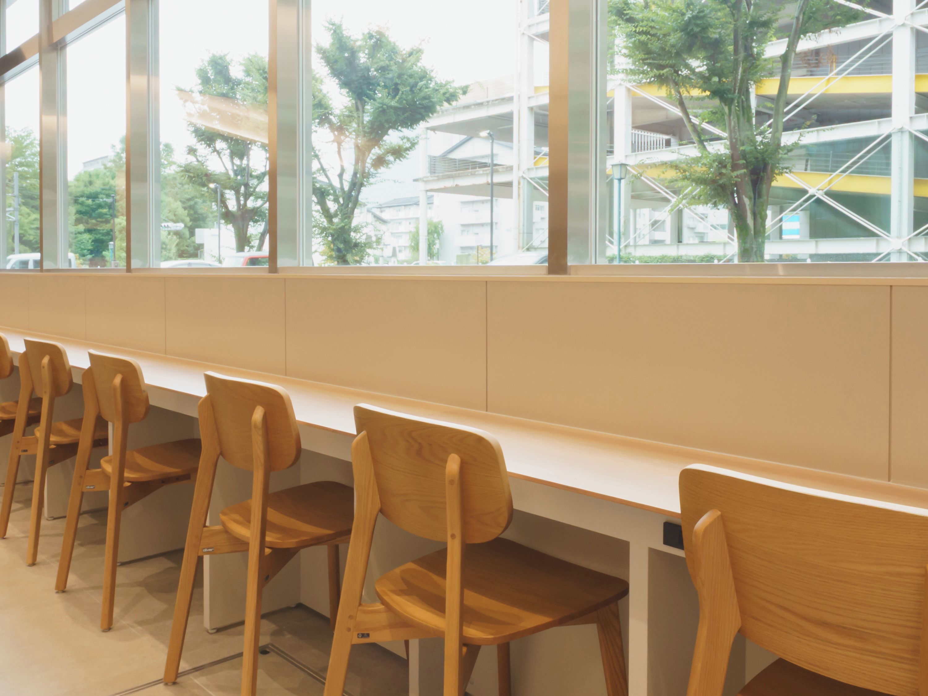 A row of wooden chairs with a white table in a modern indoor setting with large windows.