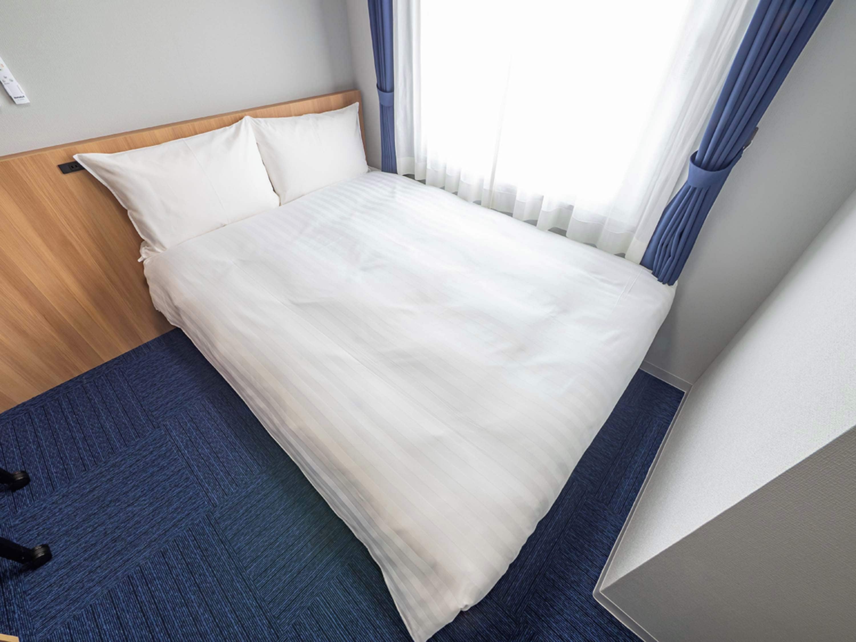 Una cama bien hecha con sábanas blancas, un cabecero de madera y un suelo cubierto de moqueta azul.