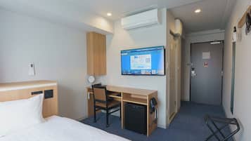 Une chambre d’hôtel comprenant un lit, un bureau avec une chaise, un petit réfrigérateur, un téléviseur à écran plat fixé au mur et une porte avec une poignée.