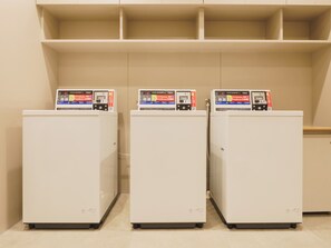 Three white refrigerators with boxes on top, placed against a wall with shelves above. - Toyoko Inn Tsukuba-eki (Tsukuba)