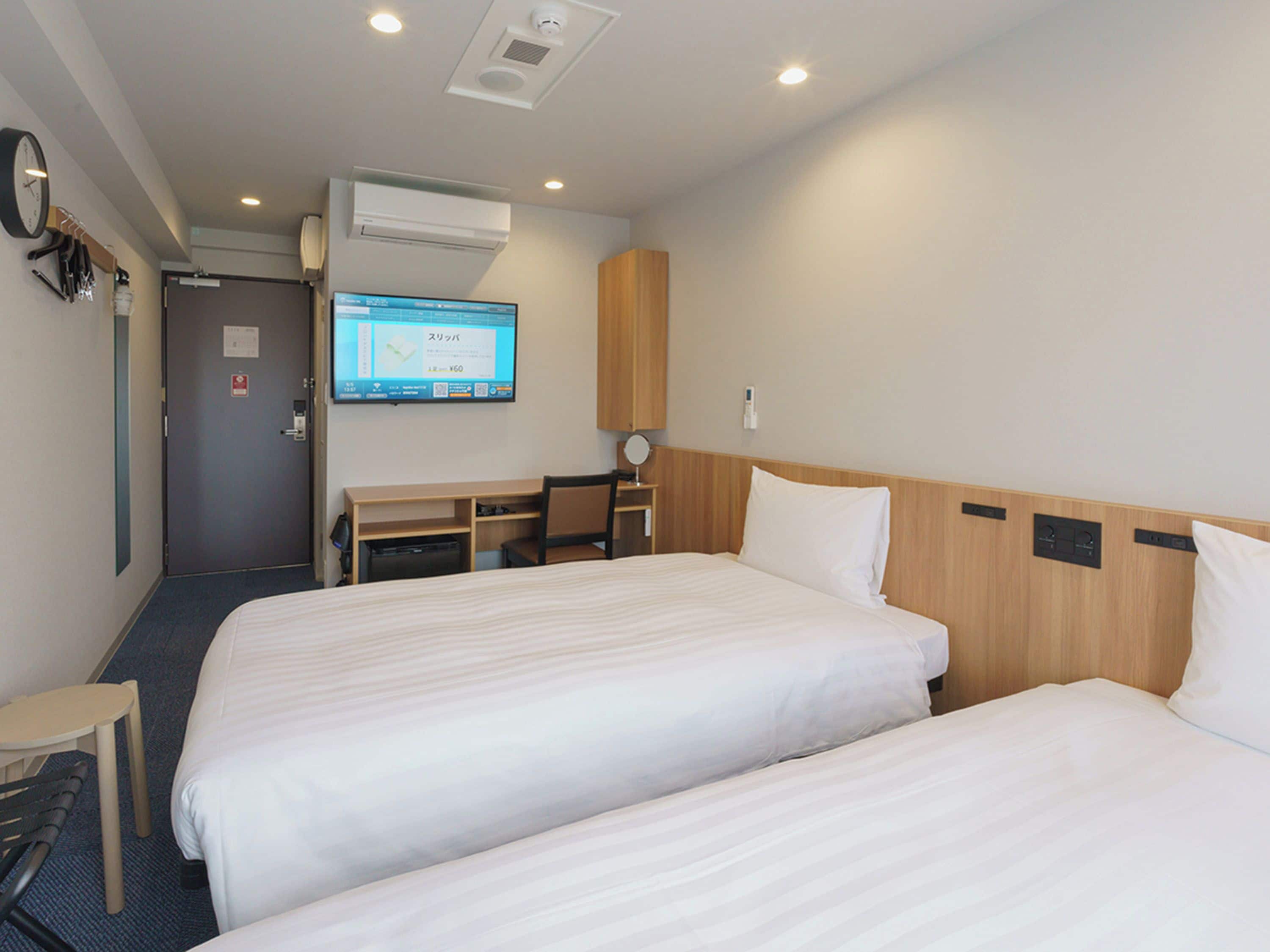 A hotel room with two beds, a desk, a chair, a television, and an air conditioning unit.