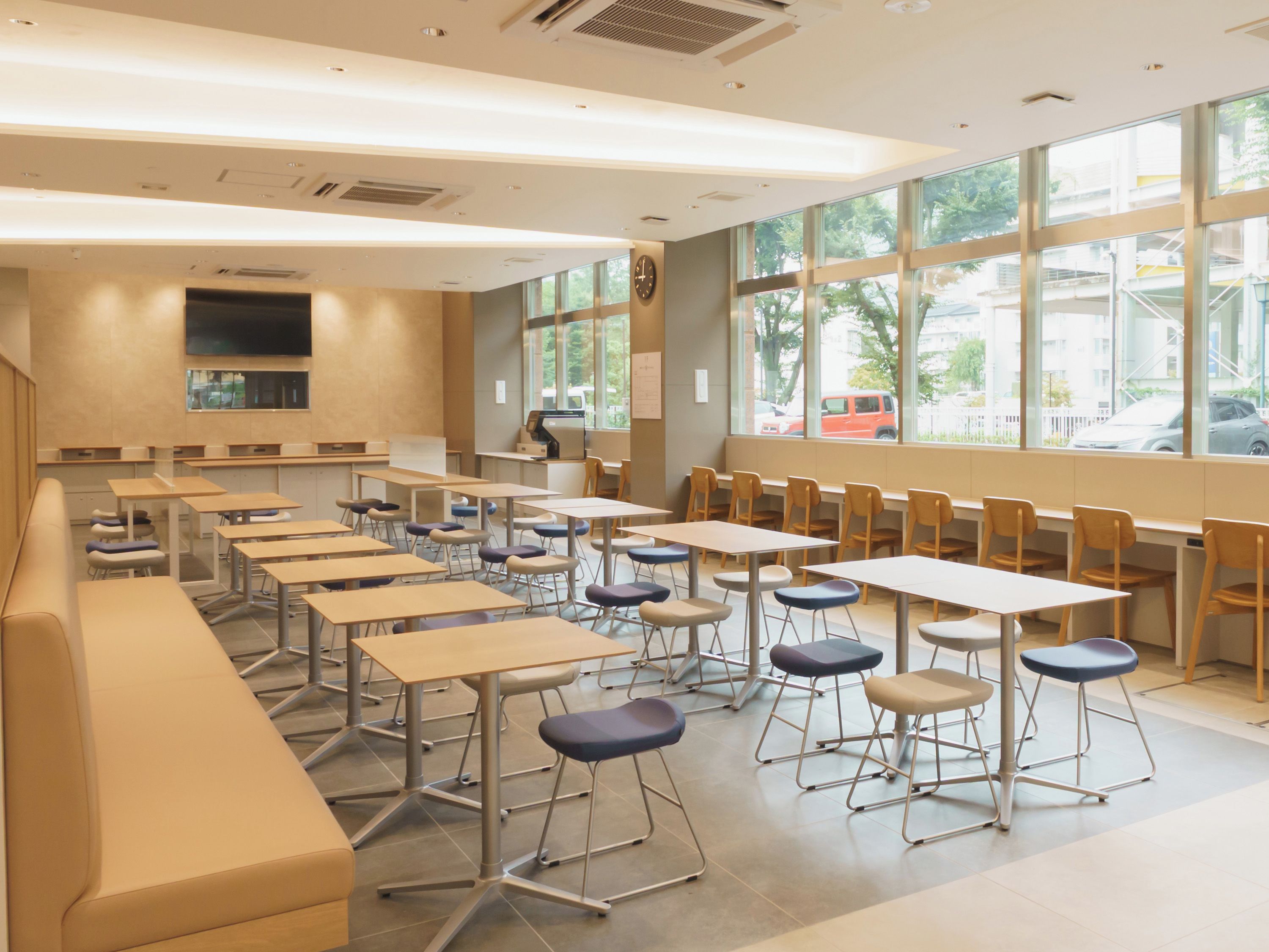 A classroom with multiple tables and chairs, large windows, and a clock on the wall.