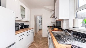 Et moderne køkken med hvide skabe, en træbordplade, indbygget ovn og en stålvask.