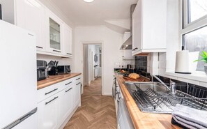 Une cuisine moderne avec des meubles blancs, un plan de travail en bois, un four encastré et un évier en acier inoxydable.