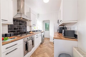 A compact kitchen with white cabinets, a wooden countertop, a built-in oven, and a washing machine. - Charming 3-Bedroom Wolverhampton Home with Private Hot Tub (West Midlands)