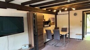 Habitación con televisión de pantalla plana, una mesa de madera, una mesa de comedor con sillas y una puerta que da a otra habitación.