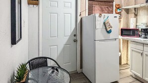 A compact kitchen with a white refrigerator, a microwave, and a small dining area with a glass table and wicker chairs. - Executive Studio (Lehigh Acres)
