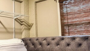 A bed with striped bedding, a tufted headboard, and a metal shelf unit against a textured wall. - Executive Studio (Lehigh Acres)