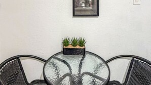 A round glass table with two black mesh chairs, a small black planter with green plants, and a framed picture on the wall. - Executive Studio (Lehigh Acres)