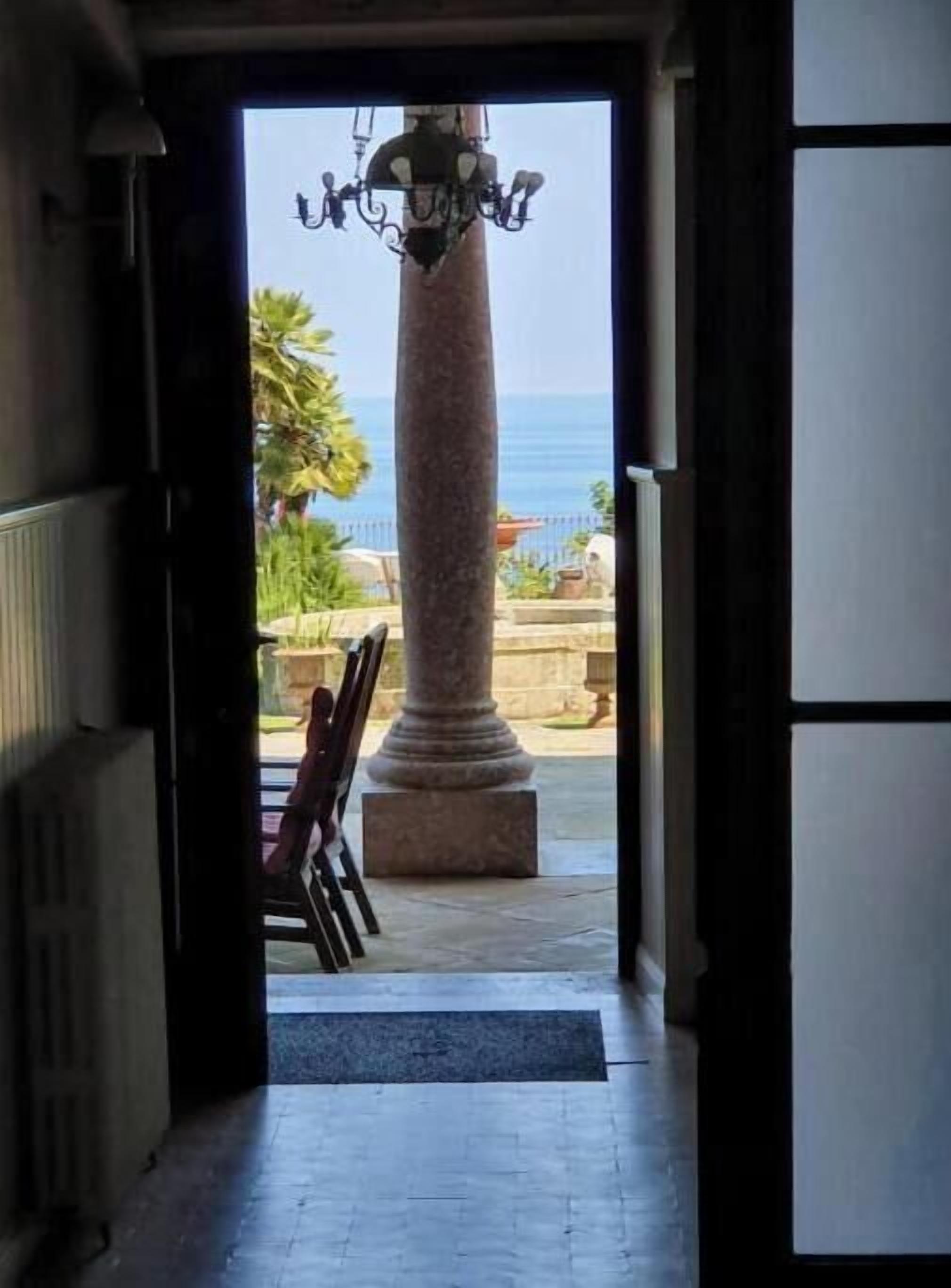 A doorway leading to an outdoor area with a view of the sea, a stone column, and a chair.