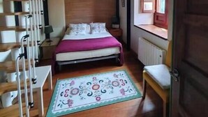 Een slaapkamer met een stapelbed, een nachtkastje, een stoel, een raam met uitzicht en een radiator.