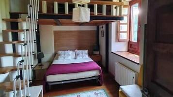 A bedroom with a bunk bed, a bedside table, a chair, a window with a view, and a radiator.