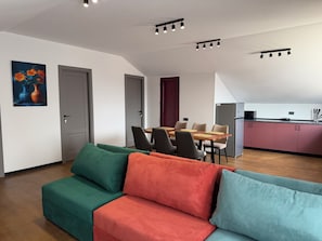 Een moderne woonkamer met een bank, een eethoek met stoelen, een keuken met kastjes en een schilderij aan de muur.