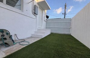 A white house with a small front yard, a hose, and a wooden fence. - Miami Enchanted Studio (Miami Gardens)