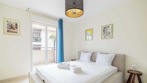 Ein ordentlich gemachtes Bett mit weißen Leinen und Handtüchern, ein Nachttisch mit Lampe sowie ein Balkon mit blauen Vorhängen.
