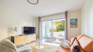 Ein modernes Wohnzimmer mit Sofa, Sessel, Fernseher und einer Glastür zum Außenbereich.