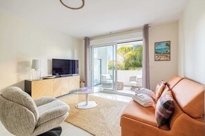 Ein modernes Wohnzimmer mit Sofa, Sessel, Fernseher und einer Glastür zum Außenbereich.
