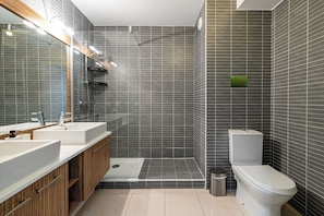Ein modernes Badezimmer mit Dusche, zwei Waschbecken, Toilette und Spiegel.