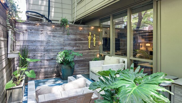 Une terrasse dotée de meubles en osier, de plantes en pot et d’un mur en bois.