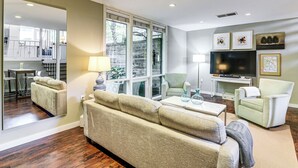 Un salon comprenant un canapé, des fauteuils, un téléviseur et un coin repas visible à travers une porte vitrée.