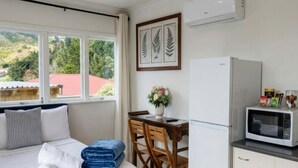 A bedroom with a bed, a dining table with chairs, a microwave, and a refrigerator. - Cosy Studio Retreat in Porirua. perfect for a peaceful getaway or business trip. (Porirua)