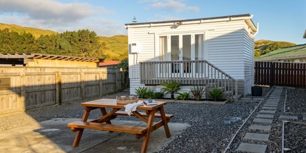 Une maison blanche avec un balcon, une table de pique-nique en bois et une allée gravillonnée.