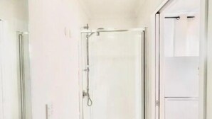 A bathroom with a shower, a mirror, and a door leading to another room. - Cosy Studio Retreat in Porirua. perfect for a peaceful getaway or business trip. (Porirua)