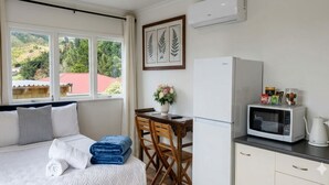 A bedroom with a bed, a desk, a chair, a window with a view, a refrigerator, and a microwave. - Cosy Studio Retreat in Porirua. perfect for a peaceful getaway or business trip. (Porirua)