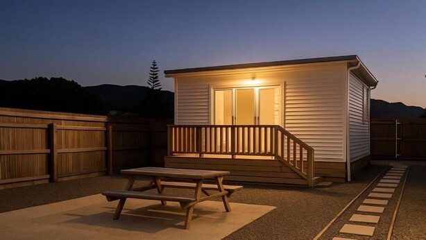 A small, single-story building with a wooden deck and a picnic table in the foreground. - Cosy Studio Retreat in Porirua. perfect for a peaceful getaway or business trip. (Porirua)