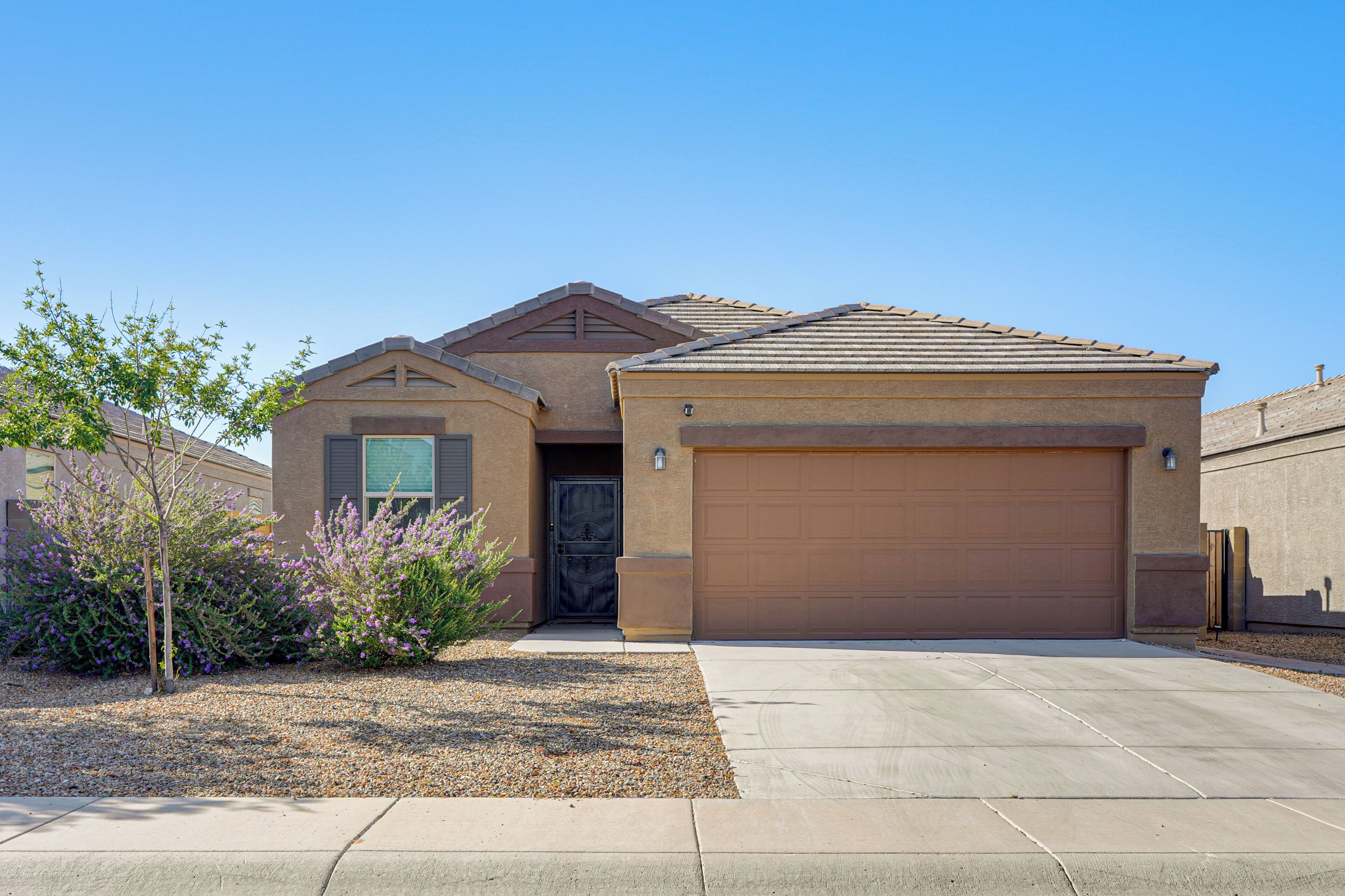 A residential house with a garage, a driveway, and a small garden with shrubs.