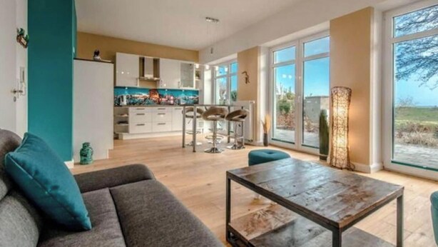 A modern living room with a sofa, a coffee table, and a view of a kitchen and dining area. - Ferienwohnung in Orth auf Fehmarn (Fehmarn)