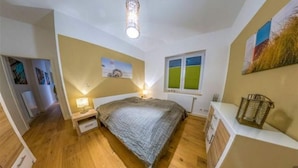 A bedroom with a bed, bedside tables, a window, and a wall-mounted artwork. - Ferienwohnung in Orth auf Fehmarn (Fehmarn)