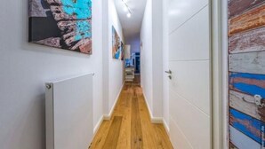 A narrow hallway with wooden flooring, white walls, and a door with a rustic, painted exterior. - Ferienwohnung in Orth auf Fehmarn (Fehmarn)