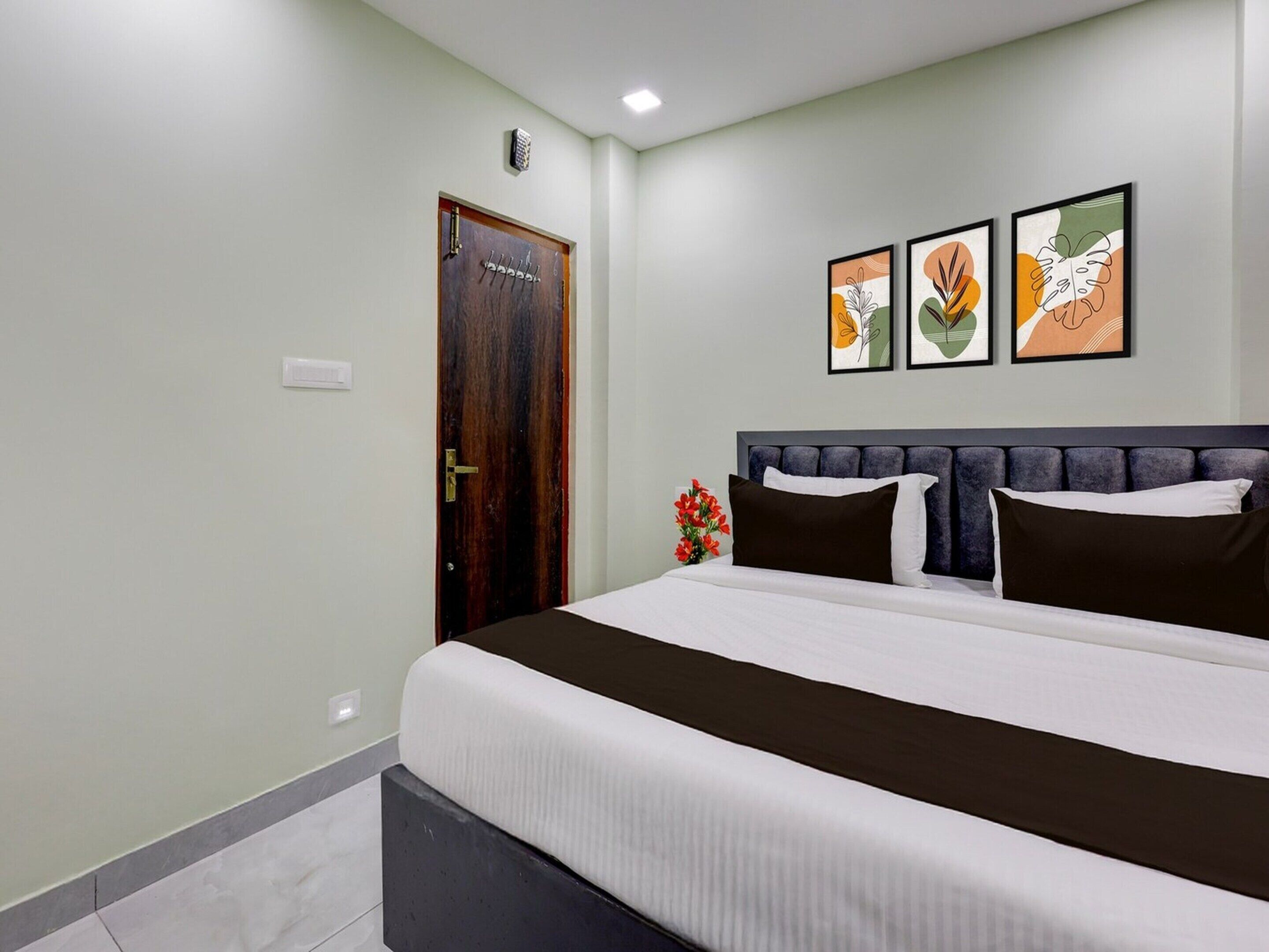 A bedroom with a bed, a wooden door, and three framed artworks on the wall.
