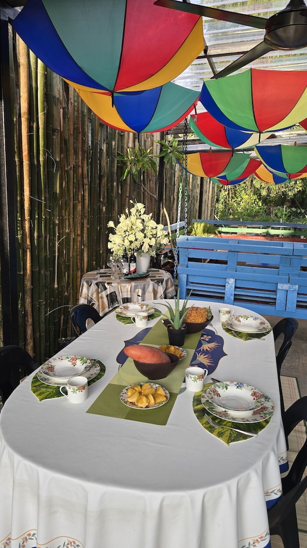 An outdoor dining area with a table set for two, surrounded by bamboo walls and a blue bench.