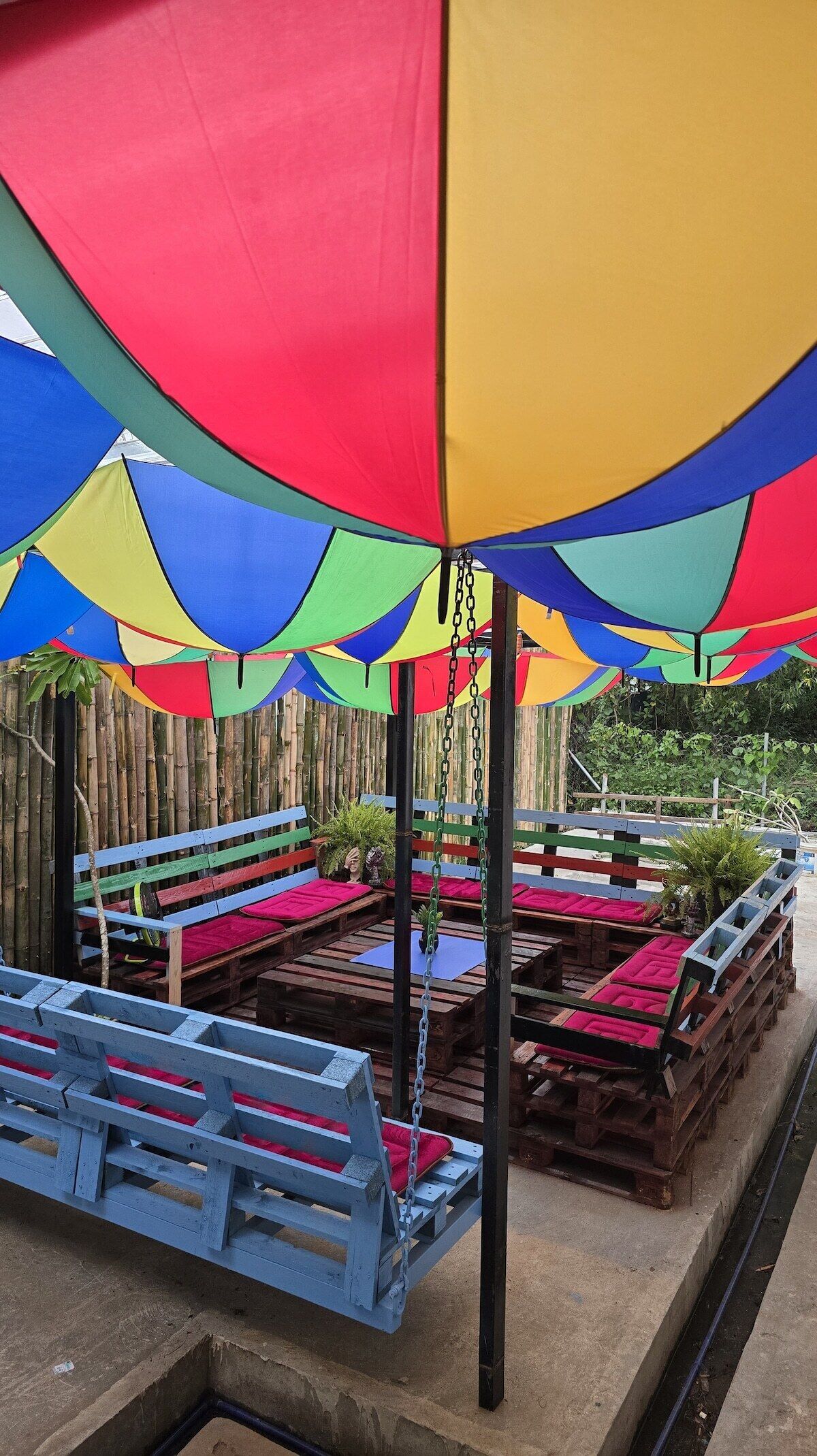 A covered outdoor seating area with wooden benches and tables, surrounded by a bamboo fence.