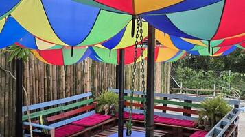A covered outdoor seating area with wooden benches and tables, surrounded by a bamboo fence.
