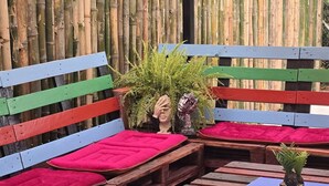 A wooden bench seating area with a bamboo backdrop, a small table with a potted plant, and colorful fabric canopies overhead. - Tuaran Kampung Villa | Near Dalit Beach & River (Tuaran)