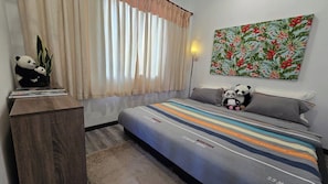 A bedroom with a bed, pillows, a lamp, a wall art, and two stuffed pandas.
