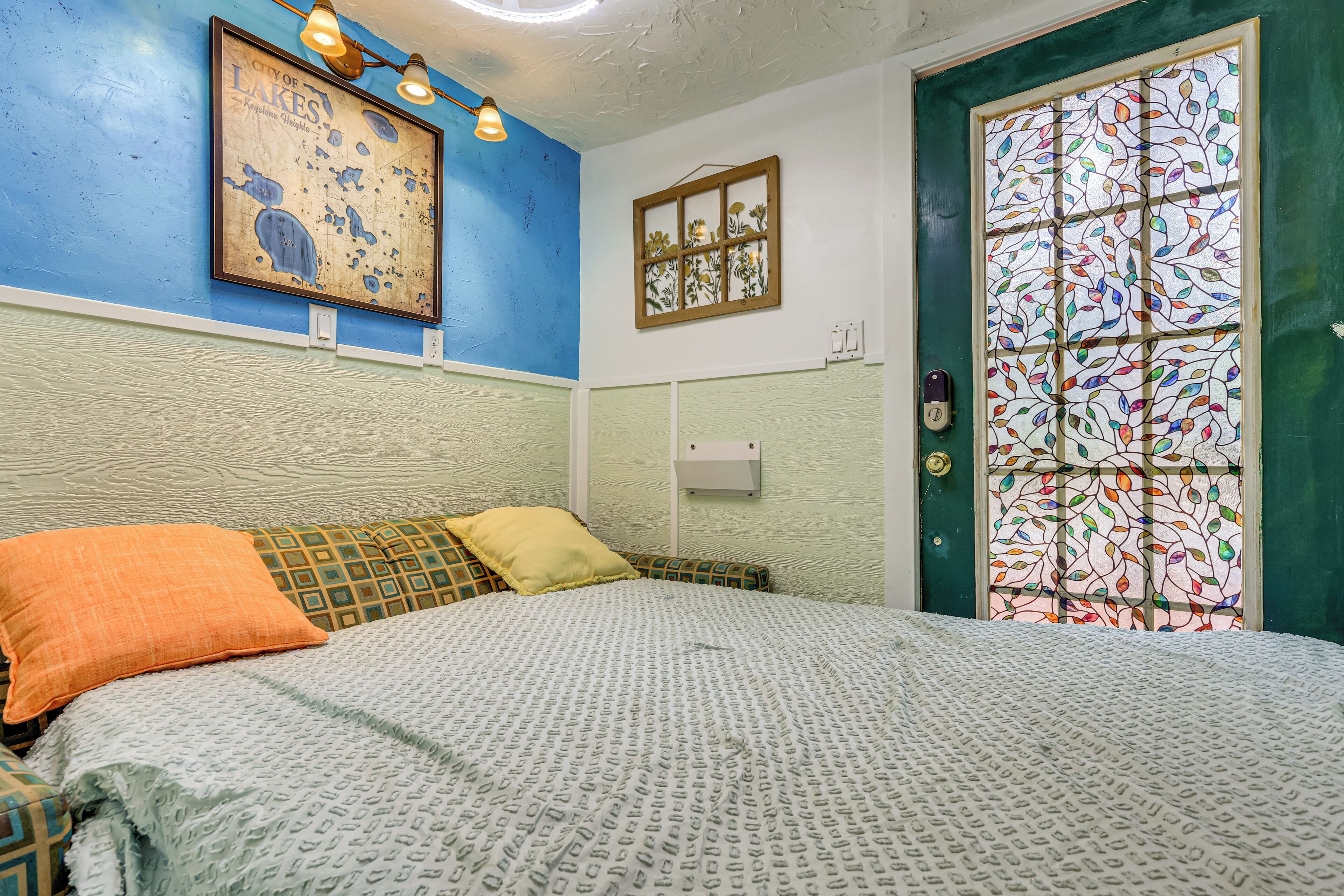 A room with a bed, a framed map on the wall, a window with a stained glass design, and a door with a keyhole.